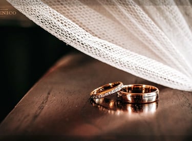 Alliances or rose et diamants sous voile de mariée en tulle, bois sombre.