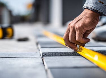 A contractor uses a yellow measuring tape to align grey stone pavers for a patio installation.