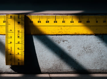 Yellow measuring tape and ruler on a concrete construction surface with dramatic shadows.