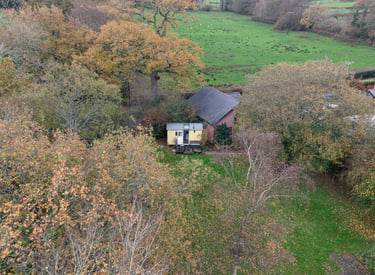 Aerial view of a yellow shepherd hut tucked into an autumn forest near a green meadow.