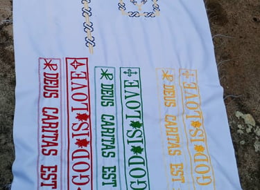 Hand-embroidered white linen featuring Deus Caritas Est and God is Love in colorful cross-stitch patterns.