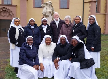 A group of Catholic nuns in white habits and winter coats posing with two seniors outside a church.