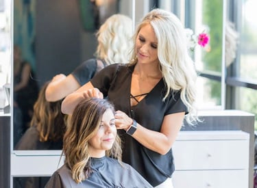 Professional blonde hair stylist styling a client's brunette hair at a modern hair salon.