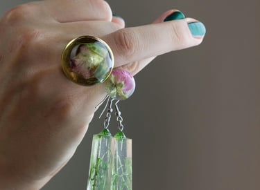 UN llaveros de resina colgando de UN dedo de la Mano de una persona que tiene un anillo con un cuarso Verde y dorado