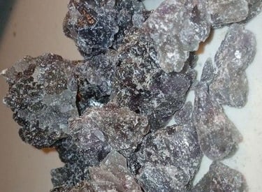 Raw chunks of dark purple and black MDMA crystals, also known as Molly, on a white surface.