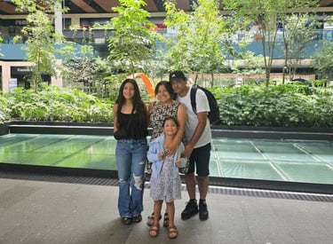 A family of four poses together in a modern outdoor shopping mall with lush green plants.