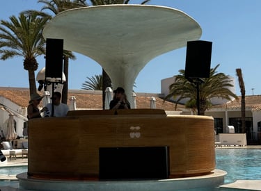 Dj booth - Kat Bendis performing at Destino Ibiza luxury resort swimming pool with palm trees.