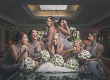 Smiling bride and bridesmaids in grey dresses holding white gerbera daisy bouquets at a wedding reception.