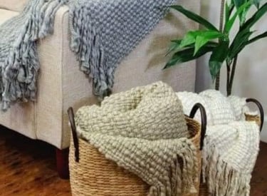 Textured knit throw blankets in a woven seagrass storage basket next to a modern sofa.