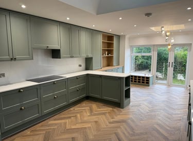 Modern sage green shaker kitchen cabinets with white marble countertops and oak herringbone flooring.