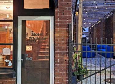 Entrance of Hotel Nichols with a glass door, brick facade, and adjacent patio area with string lights.