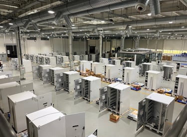 Wide view of an industrial manufacturing facility with rows of white electrical control cabinets.
