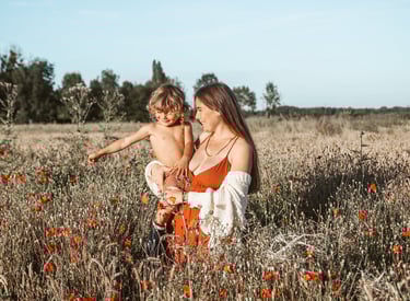 photo d'une maman en robe rouge portant son enfant torse nu dans un champ de coquelicots