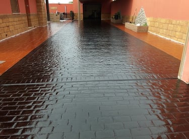Superficie de hormigón decorativo con acabado de resina y pintura en tonos oscuros, ideal para entradas y patios.