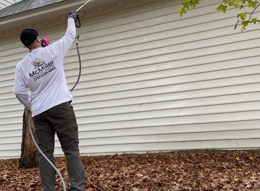 Professional contractor soft washing white house siding and roof to remove algae and stains.