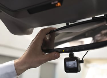 Dashcam debajo de un espejo retrovisor y la mano de un hombre acomodandola