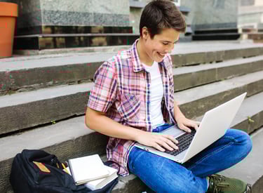 estudiante con camisa roja y pantalon azul sonriendo mientras usa una laptop para la escuela