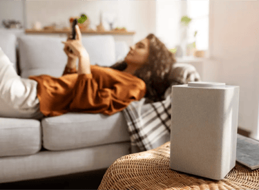 Mujer sentada en un sillón viendo su celular con un purificador de aire en primer plano