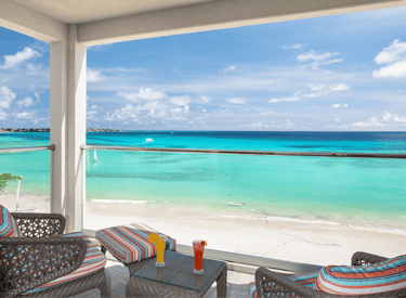 Luxury resort balcony overlooking a tropical turquoise beach with cocktails on a table.