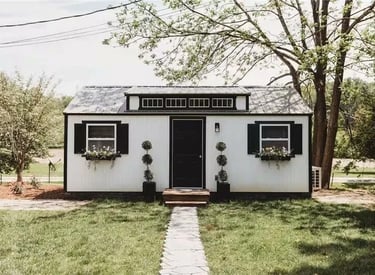 Custom she shed with white LP SmartSide® siding, black trim, and flower boxes in a landscaped yard