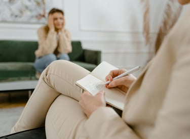Distressed woman sitting on a couch in an office with a therapist who is taking notes