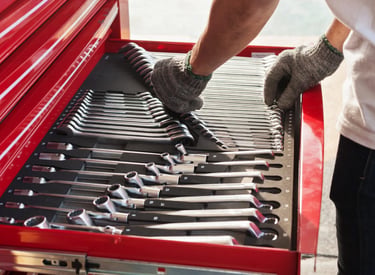 A red toolbox with organized wrenches, with a mechanic wearing gloves reaching for a tool.