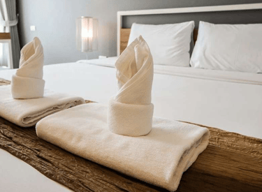 Quarto de hotel com cama branca cuidadosamente feita, mostrando um ambiente limpo e acolhedor