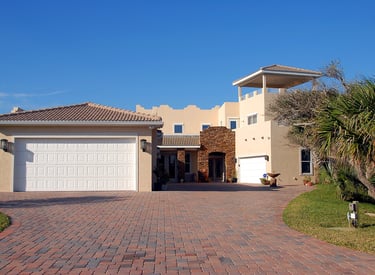Beautiful Mediterranean-style house with tan stucco exterior, terracotta-tiled roof, and brick-paved