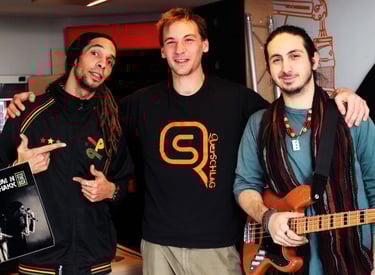 three men standing next to each other producing songs , one is holding a guitar