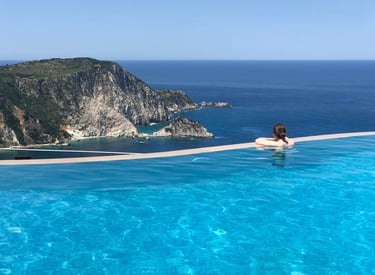 Person relaxing in a luxury infinity pool overlooking a rugged coastal cliff and blue ocean.