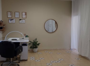 עמדת מניקור בסטודיו SBS – חלל עבודה אלגנטי ומואר עם מראה עגולה וצמח ירוק.