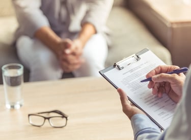 Zwei Personen in einer Psychotherapiesitzun. Der Psychotherapeut macht sich Notizen.