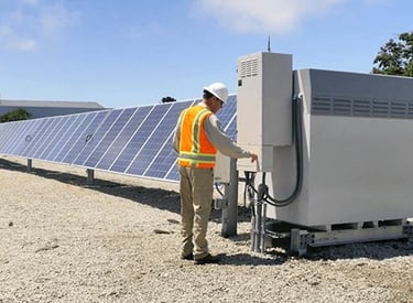 A technician inspecting solar panels and an inverter system at a renewable energy farm.