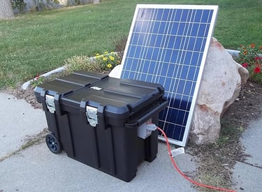 Portable solar power generator kit with a black battery case and solar panel set up outdoors.