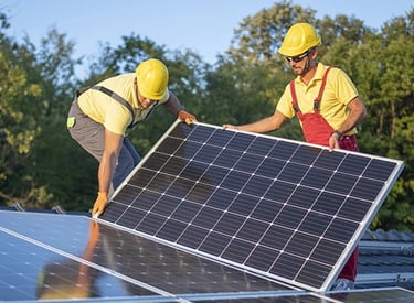 Two technicians in hard hats installing solar panels on a residential rooftop for renewable energy.