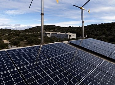 Rooftop solar panel array and small wind turbines providing renewable energy to a rural building.