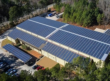 Aerial view of a large commercial solar panel installation on an industrial building roof.