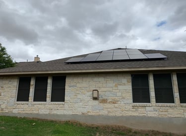 Residential rooftop solar panels installed on a stone house under a cloudy sky.