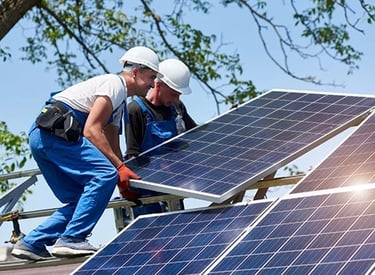 Professional solar installers in hard hats mounting photovoltaic panels on a residential rooftop.