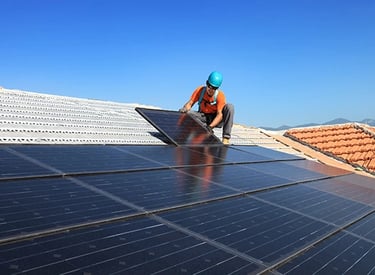 Professional contractor installing black solar panels on a residential roof under a clear blue sky.