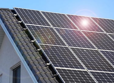 Residential rooftop solar panels installed on a tiled house roof under bright sunlight.