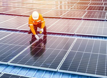 A technician in a hard hat installing solar panels on a rooftop for renewable energy.