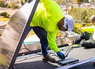 Professional technicians in safety gear installing solar panels on a residential rooftop.