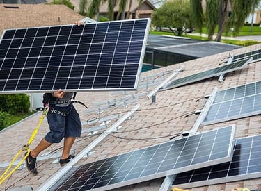 Professional technician installing a residential solar panel system on a shingle roof.