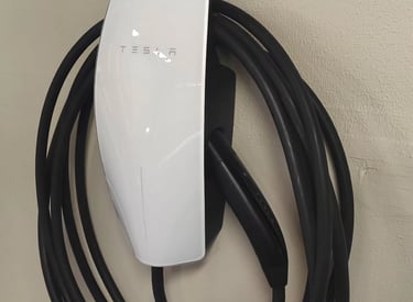 White Tesla Gen 3 Wall Connector home EV charging station mounted on a wall with cable coiled.