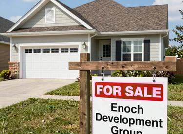 A modern, multi-story building under construction is centrally featured. The facade is primarily white, with large glass sections and several balconies. Surrounding the building are construction materials, including stacks of stone slabs. Advertising banners with colorful designs are visible on the building, and partly cloudy skies are overhead.