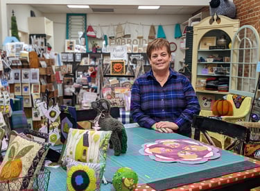 Shop owner, Cheryl, stands in front of the pattern table in The Black Sheep Wool Shop