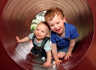 male toddler and older brother playing in play tunnel at a playground 