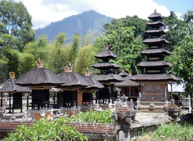 Traditional Balinese Hindu temple shrines with tiered black thatched roofs set against lush mountains.