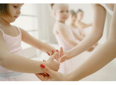 a little girl in a pink dress teacher showing girl how to hold her handsand